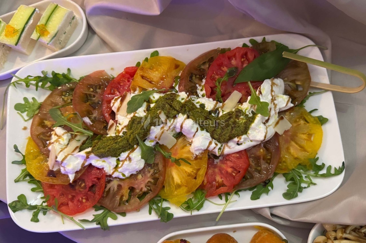 Assiette de tomates colorées avec burrata, pesto, roquette et copeaux de parmesan, présentée sur une nappe claire.