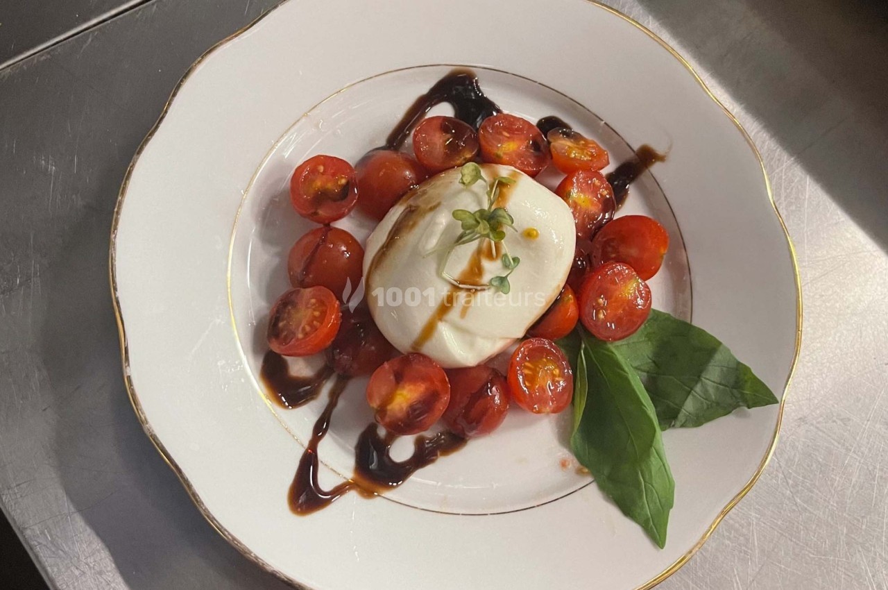 Assiette de burrata avec tomates cerises, feuilles de basilic et filet de vinaigre balsamique.