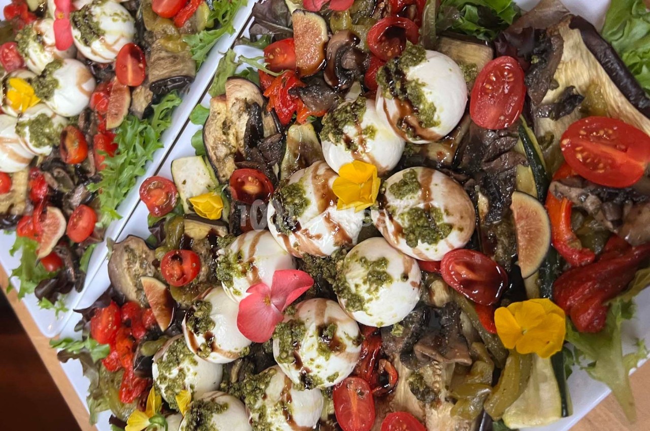 Assiette colorée composée de légumes grillés, tomates cerises, mozzarella, pesto et fleurs comestibles sur un lit de salade.