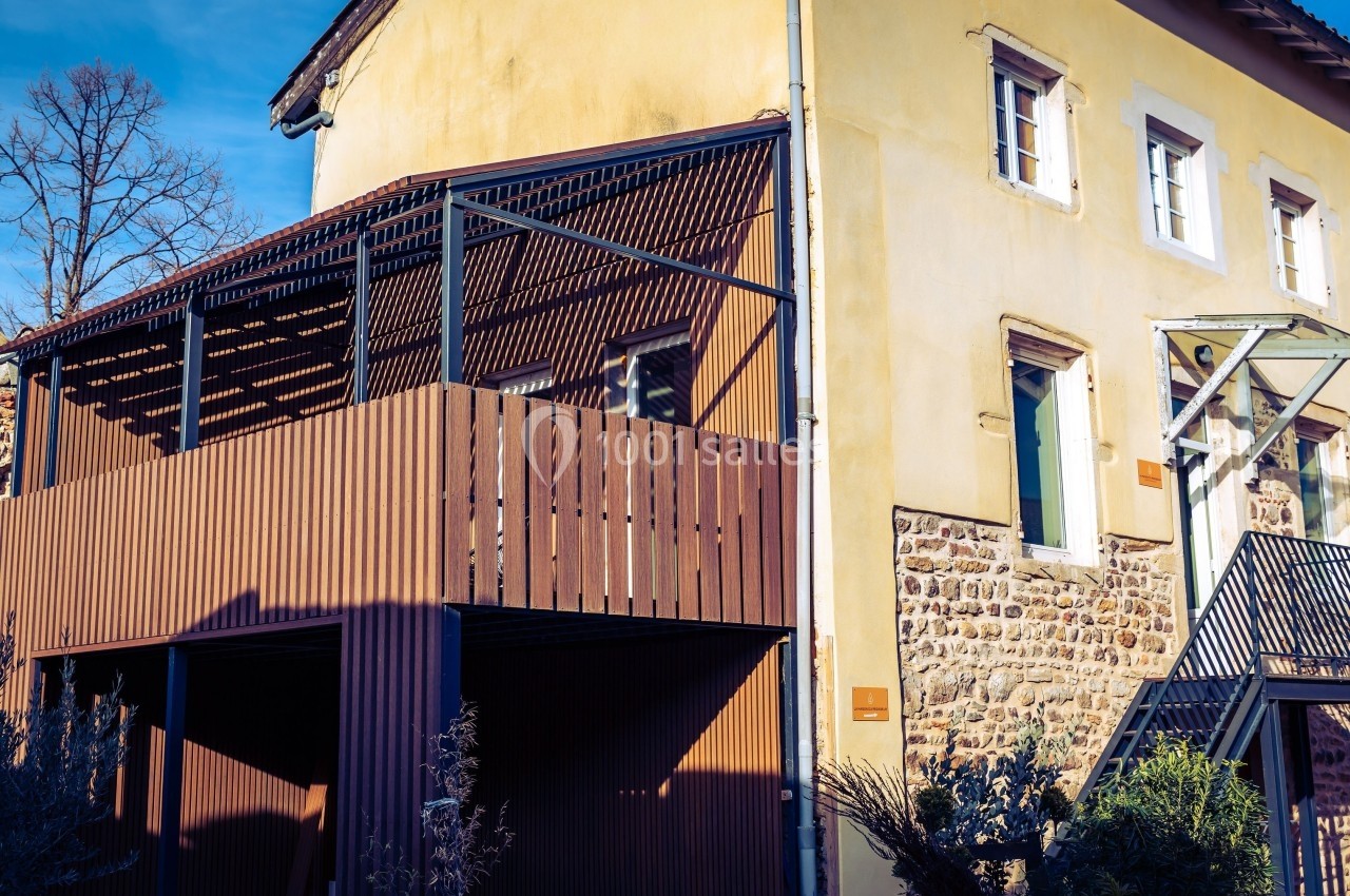 Façade d'une maison en pierre et crépi jaune avec une terrasse en bois et une structure métallique moderne.