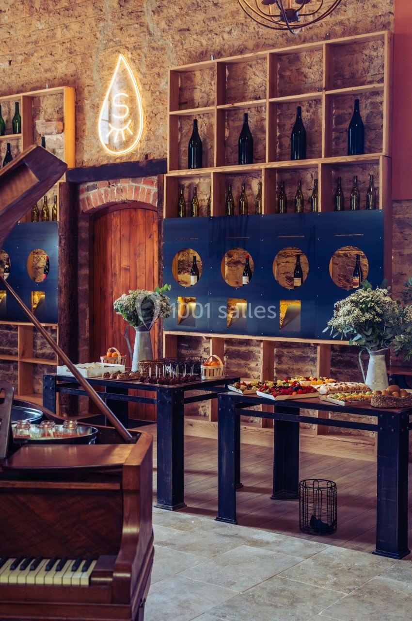 Salle décorée avec des étagères de bouteilles, un piano en bois et des tables garnies de plats et fleurs.