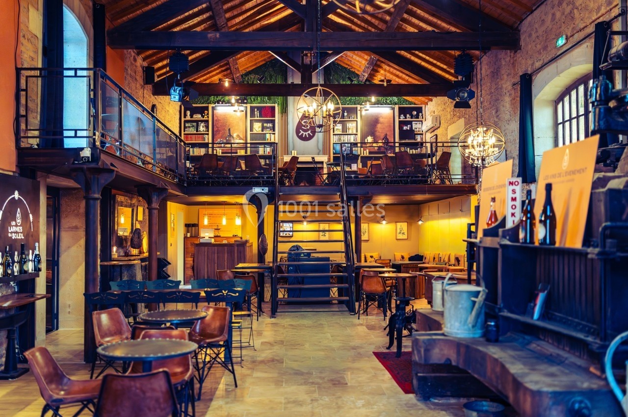 Intérieur d'un bar ou restaurant avec mezzanine, tables en bois, éclairage chaleureux et décor rustique.