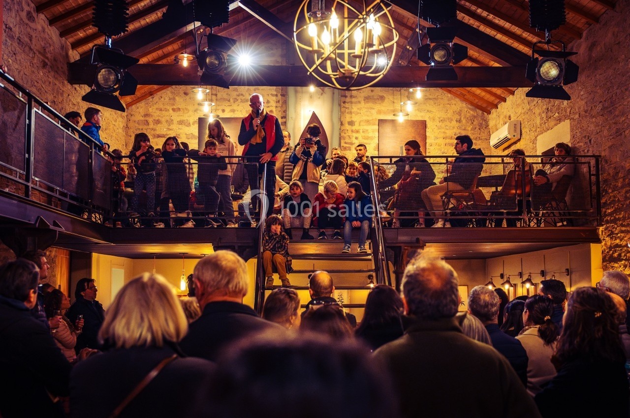 Un groupe de personnes assiste à un discours dans une salle en pierre avec mezzanine et éclairage chaleureux.
