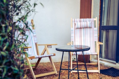 Deux chaises en rotin et une table ronde sur une terrasse ensoleillée avec des ombres marquées au sol.