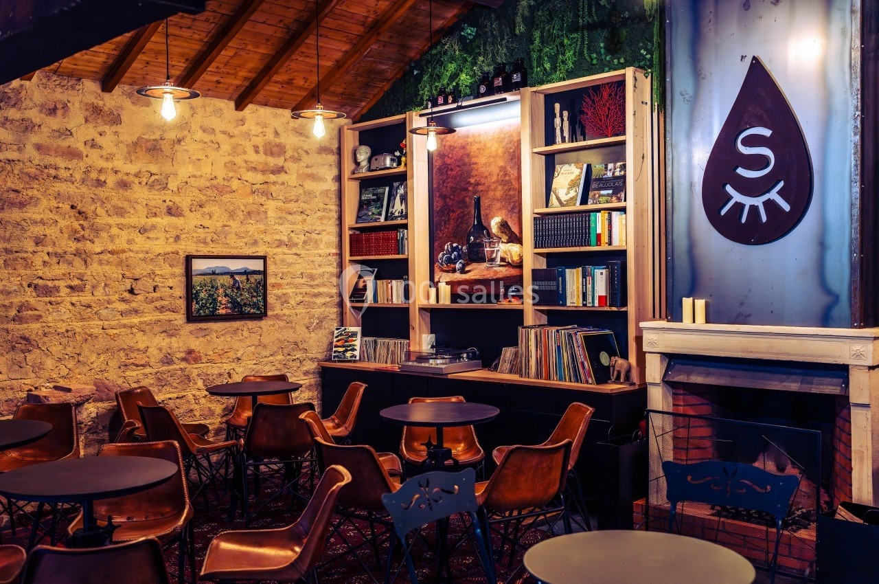 Salle de café chaleureuse avec murs en pierre, étagères remplies de livres et disques, et mobilier en bois et métal.