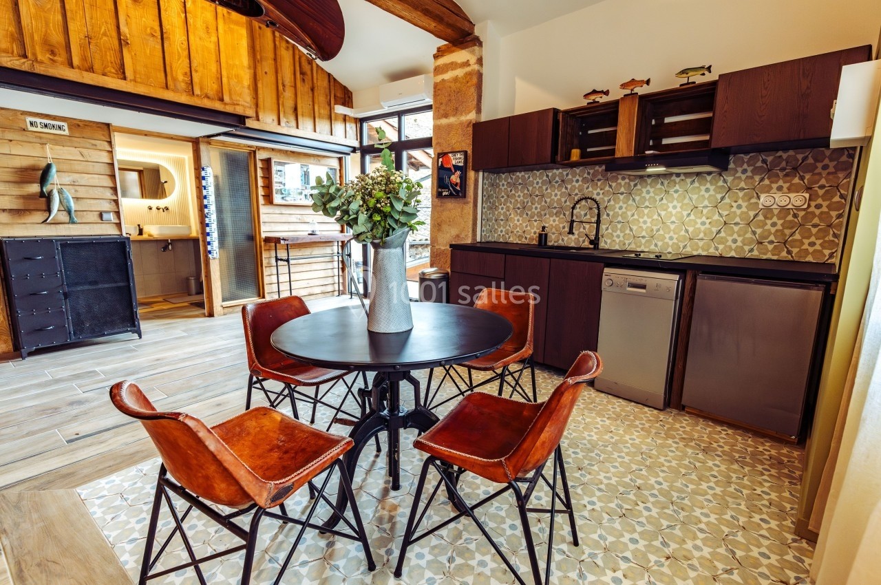 Cuisine ouverte avec table ronde, chaises en cuir, meubles en bois foncé et carrelage décoratif au sol et au mur.