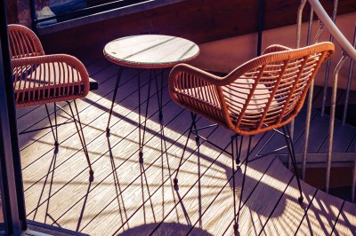 Deux chaises en rotin et une table ronde sur une terrasse ensoleillée avec des ombres marquées au sol.