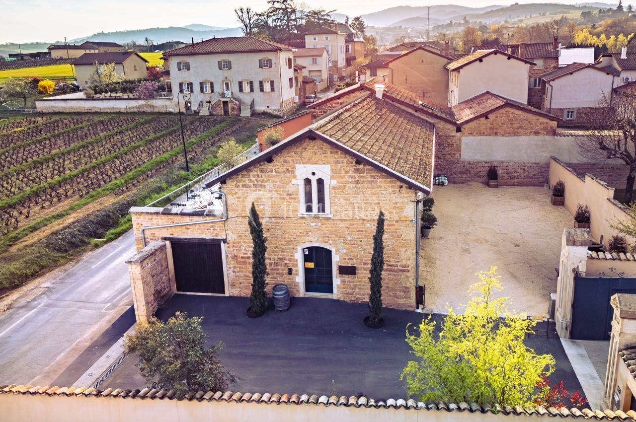 Vue aérienne d'une maison en pierre avec cour, entourée de vignes et de bâtiments dans un paysage rural ensoleillé.
