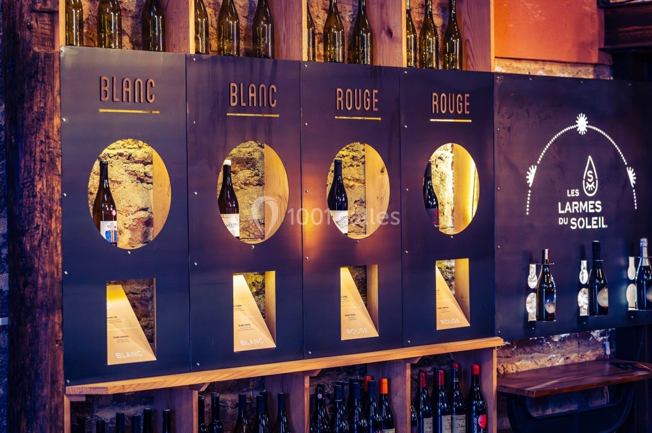 Distributeur de vin mural avec sections pour vins rouges et blancs, entouré de bouteilles sur étagères en bois.