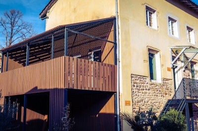 Deux chaises en rotin et une table ronde sur une terrasse ensoleillée avec des ombres marquées au sol.