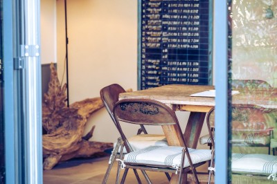 Deux chaises en rotin et une table ronde sur une terrasse ensoleillée avec des ombres marquées au sol.