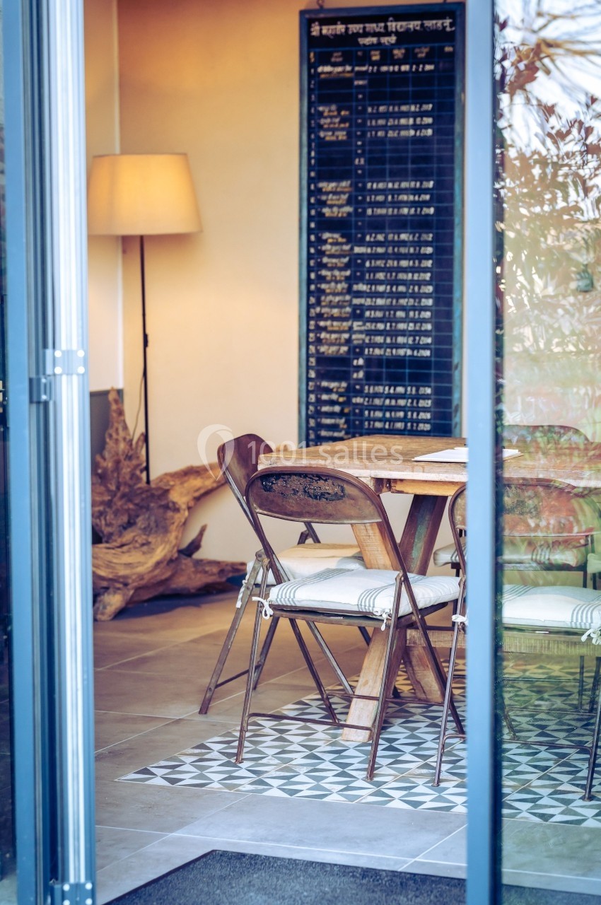 Vue d'une salle à manger avec table en bois, chaises vintage, lampe sur pied et tableau noir au mur.