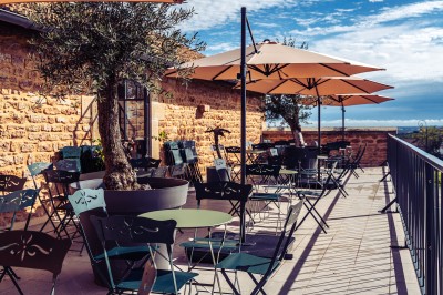 Deux chaises en rotin et une table ronde sur une terrasse ensoleillée avec des ombres marquées au sol.