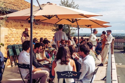 Deux chaises en rotin et une table ronde sur une terrasse ensoleillée avec des ombres marquées au sol.
