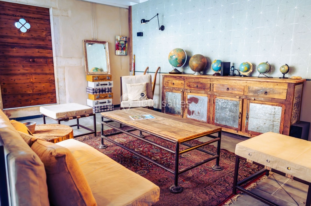 Salon vintage avec meubles en bois, globes terrestres sur un buffet, tapis ancien et fauteuils clairs.