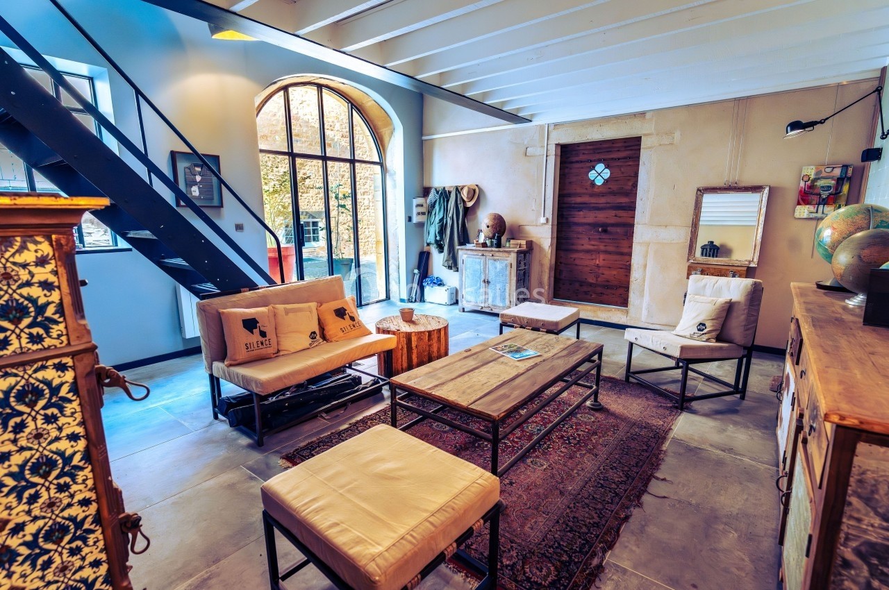 Salon lumineux avec mobilier en bois et métal, tapis au sol, grande baie vitrée et escalier en métal noir.