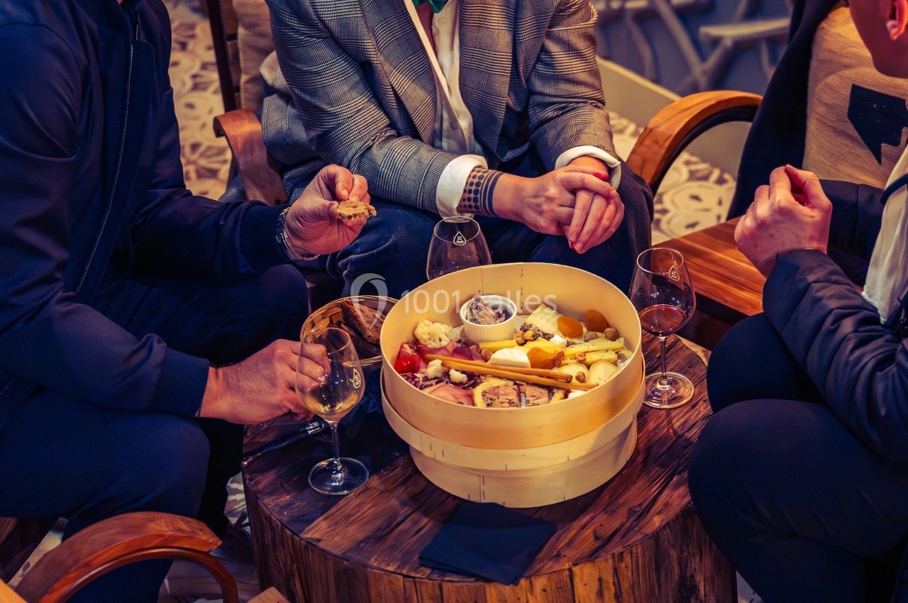 Trois personnes autour d'une table en bois dégustant un plateau de fromages et charcuteries avec des verres de vin.