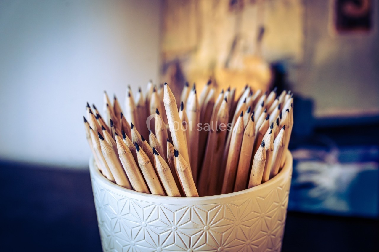 Pot blanc contenant de nombreux crayons taillés, placé sur une surface avec un arrière-plan flou.