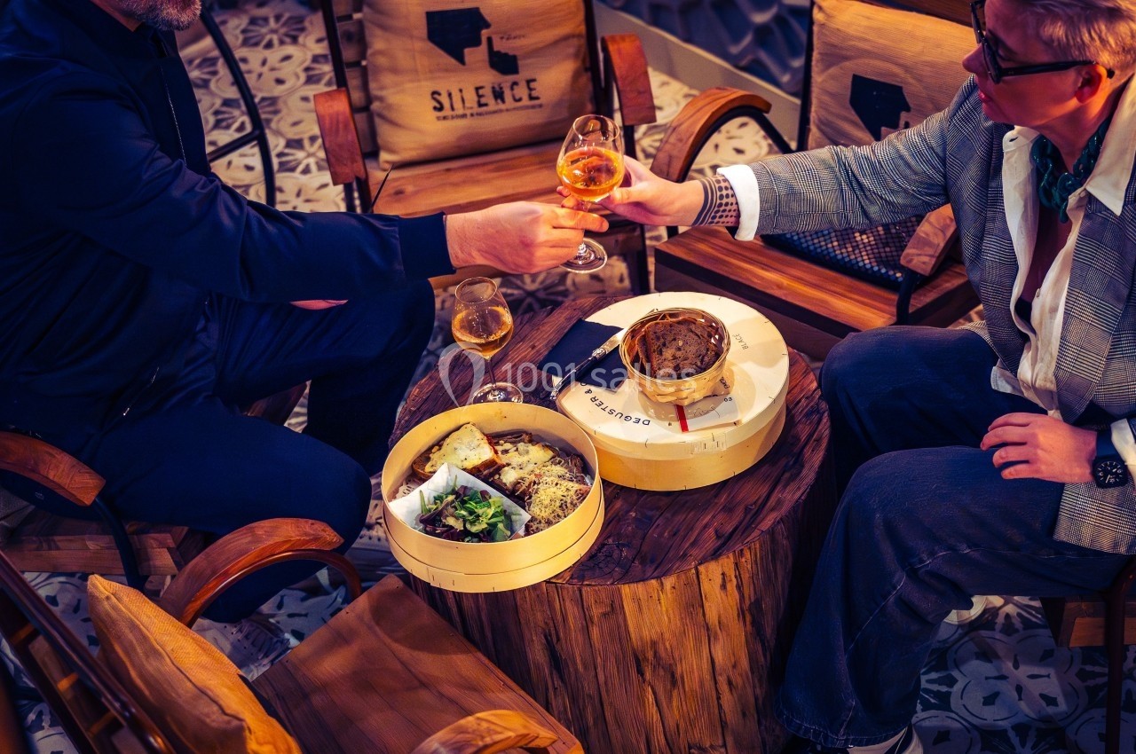 Deux personnes trinquent avec des verres de bière autour d'une table en bois garnie de plats et de paniers vapeur.
