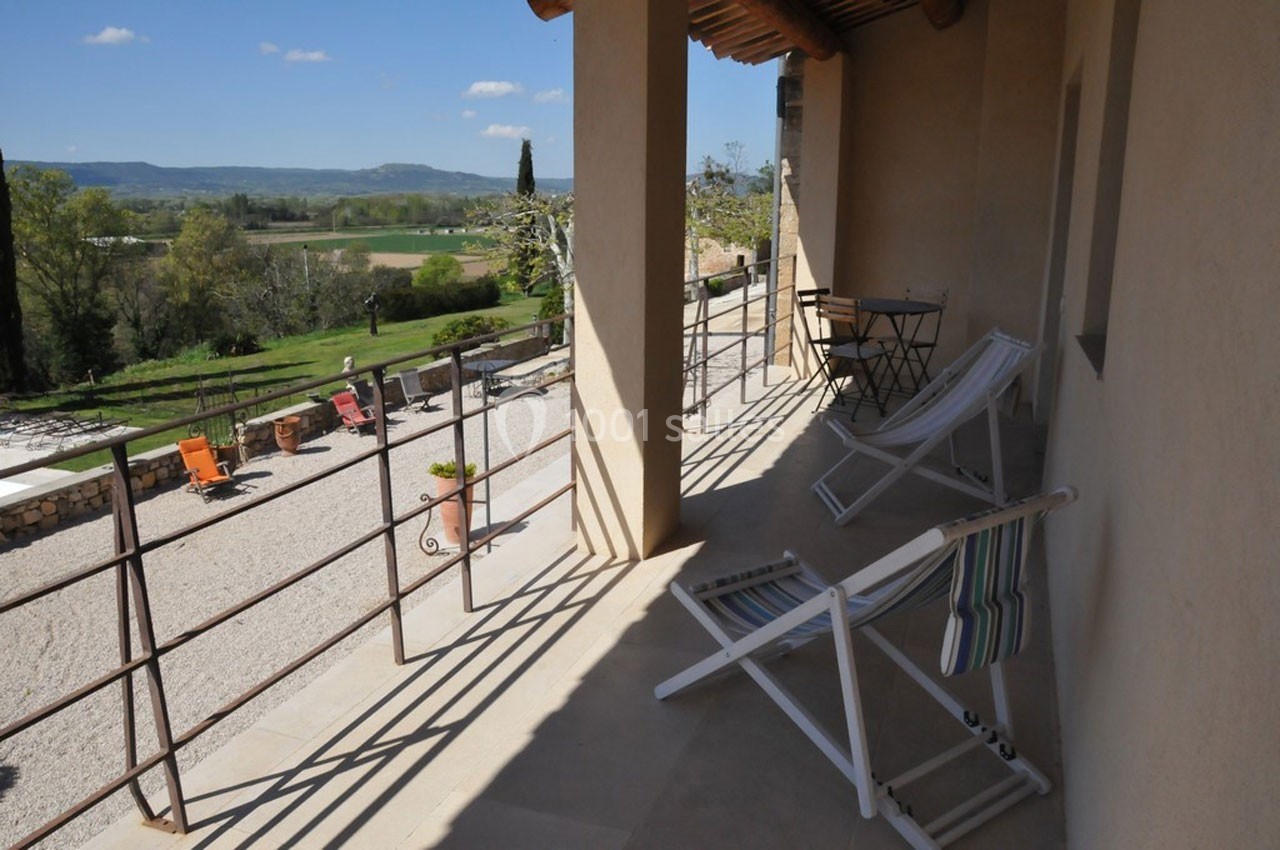 Terrasse avec transats et table, offrant une vue sur un jardin, des chaises colorées et un paysage rural verdoyant.