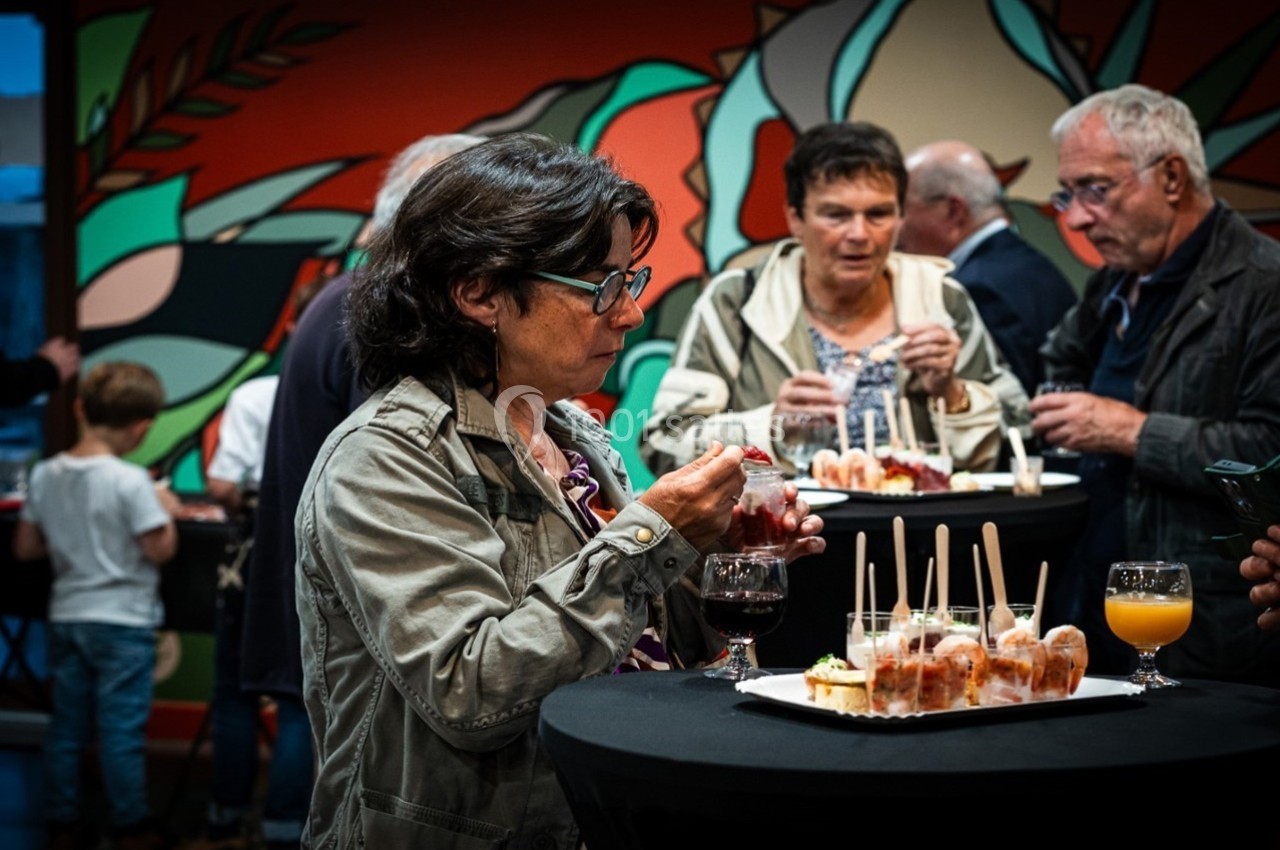 Location salle Gannat (Allier) - Paléopolis #8 Des personnes debout autour de tables hautes dégustent des amuse-bouches lors d'un événement convivial.