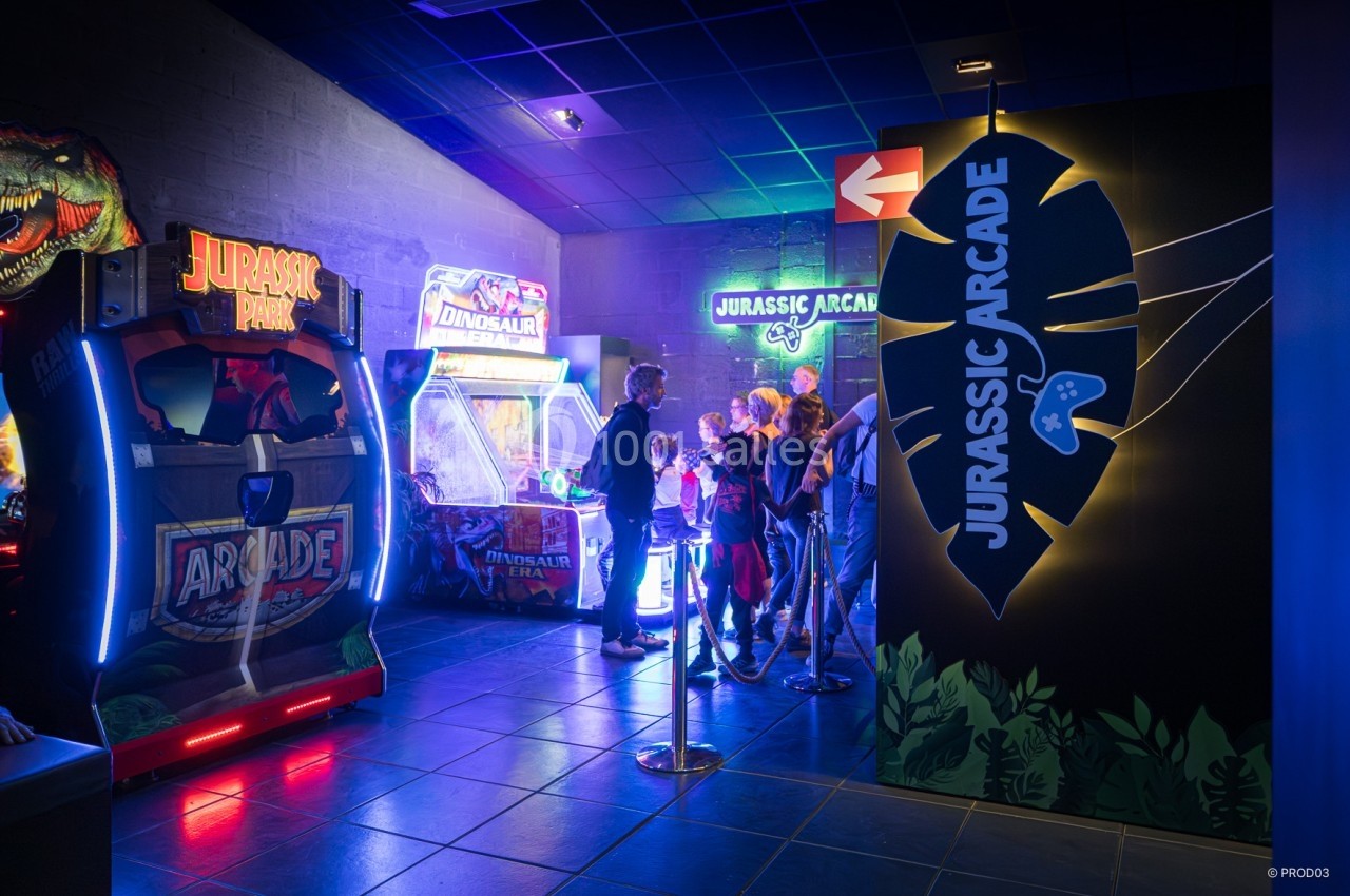 Location salle Gannat (Allier) - Paléopolis #11 Des personnes font la queue devant des bornes d'arcade dans une salle de jeux à thème Jurassic.