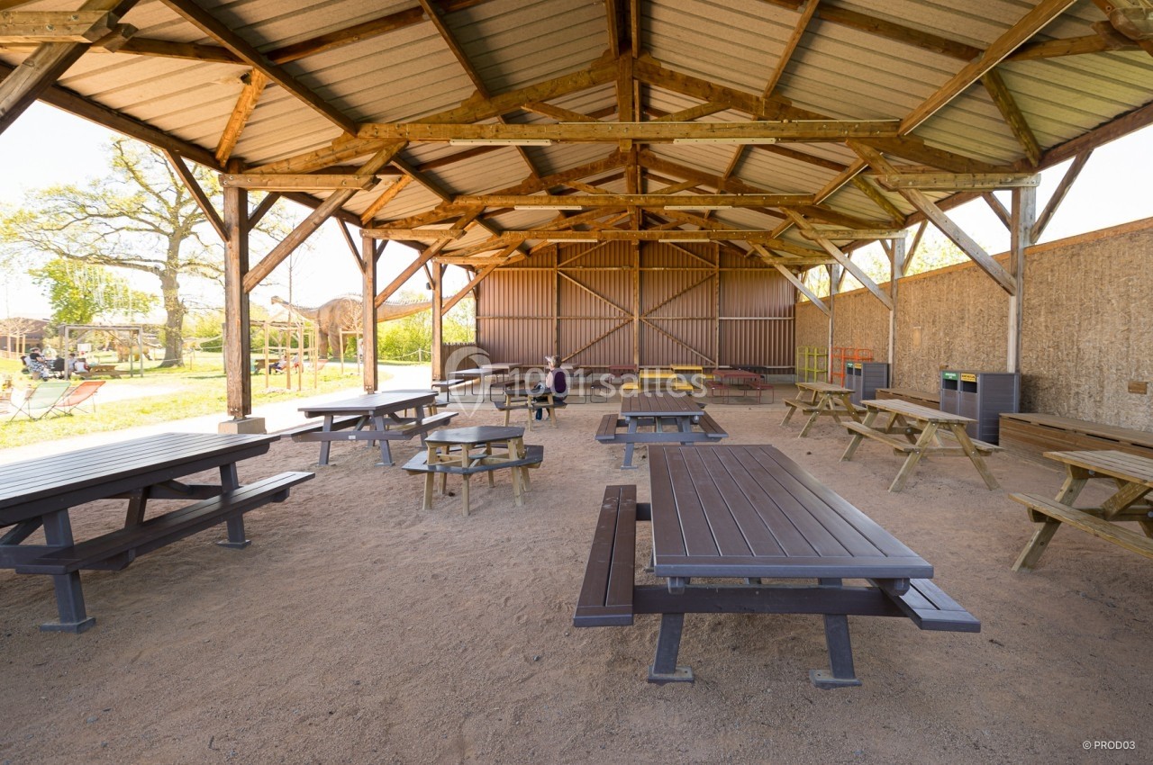 Location salle Gannat (Allier) - Paléopolis #6 Abri en bois ouvert avec tables de pique-nique, situé dans un espace extérieur ensoleillé.