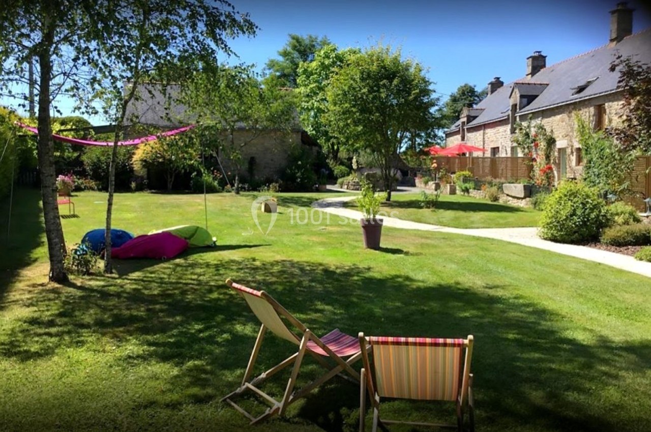 Jardin verdoyant avec chaises longues, arbres, pelouse entretenue et bâtiments en pierre en arrière-plan.