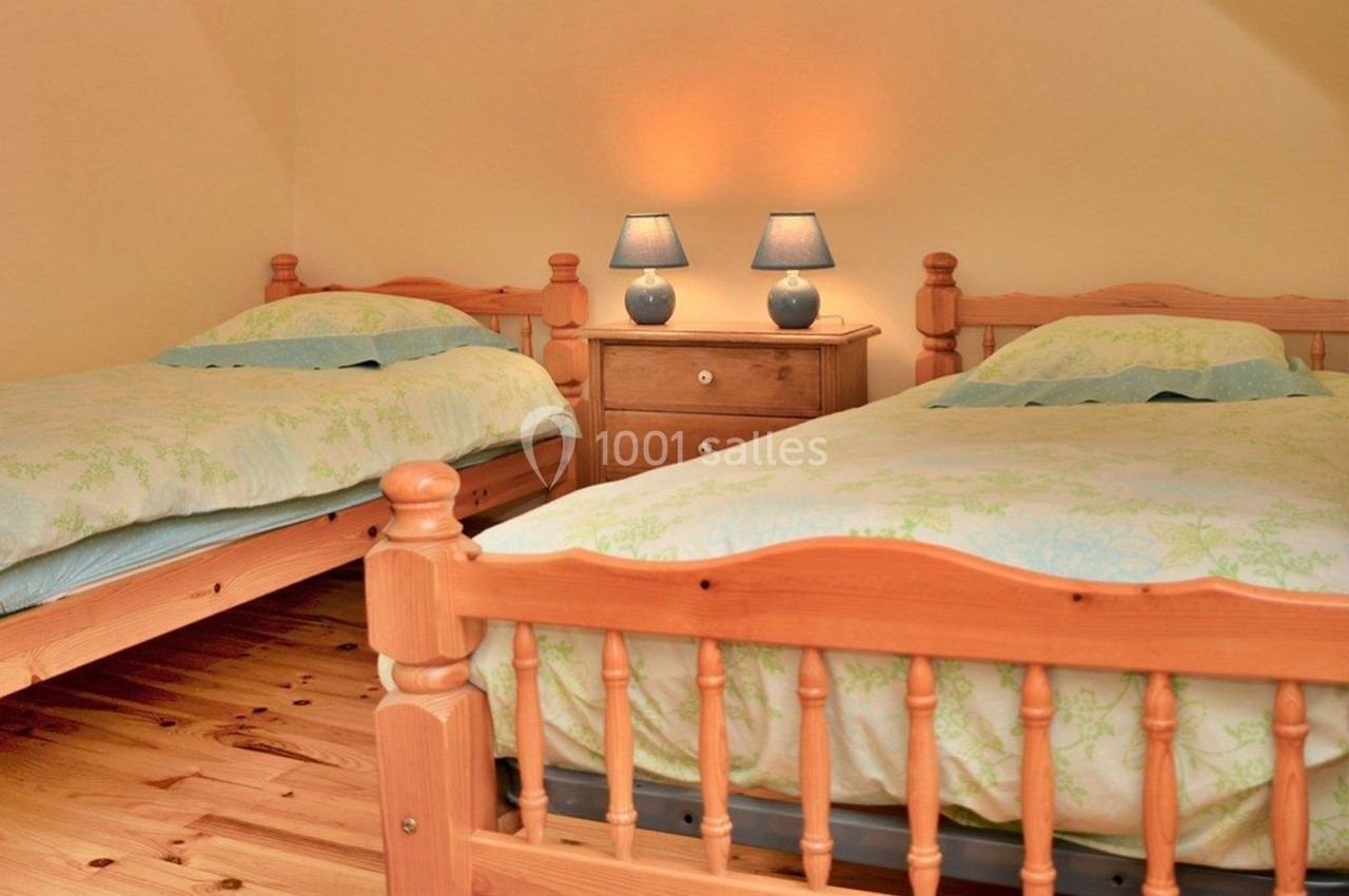 Deux lits simples en bois avec une table de chevet et deux lampes dans une chambre aux murs beige clair.