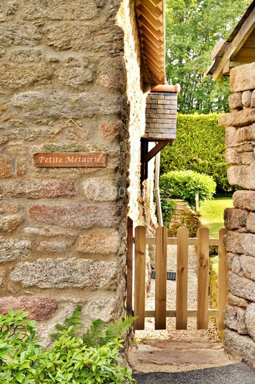 Vue d'un passage étroit entre deux murs en pierre, avec une petite barrière en bois menant à un jardin verdoyant.