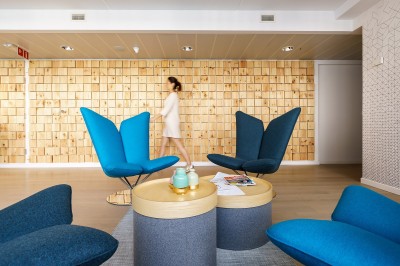 Miniature L'accueil Femme assise dans un hammam aux carreaux roses, enveloppée dans une serviette blanche.