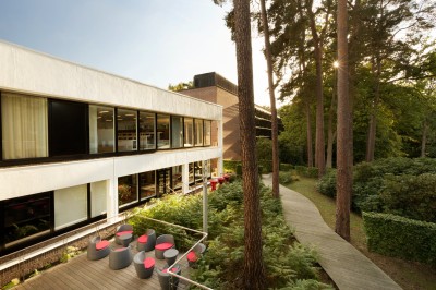 Miniature Le bâtiment du WIP Femme assise dans un hammam aux carreaux roses, enveloppée dans une serviette blanche.