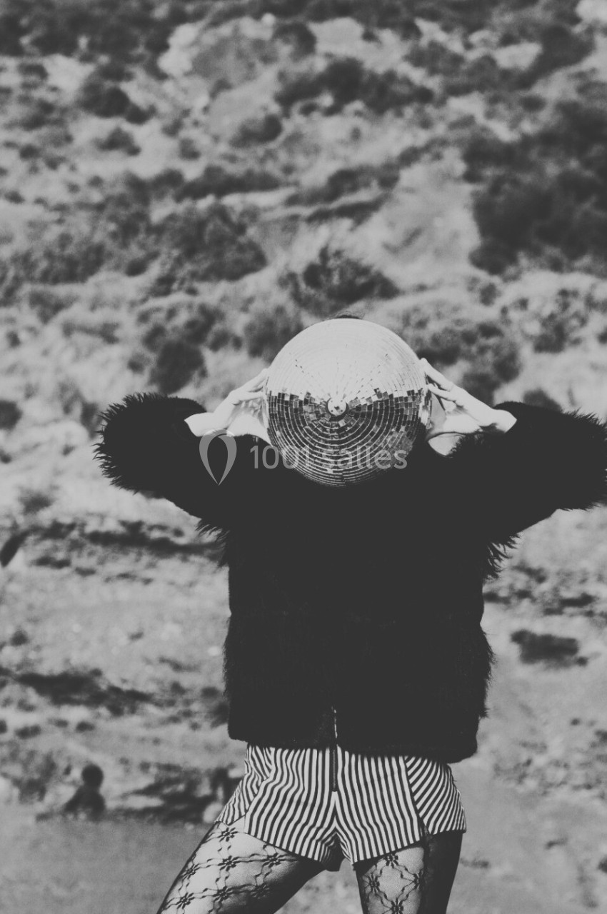 Personne portant une boule à facettes sur la tête, vêtue d'une tenue originale, dans un paysage désertique.