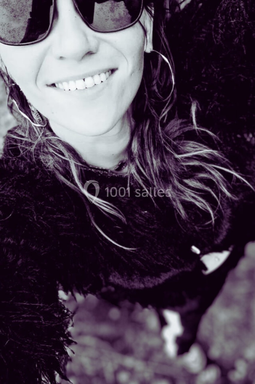 Femme souriante portant des lunettes de soleil, vue en plongée, vêtue d'un pull texturé sombre.