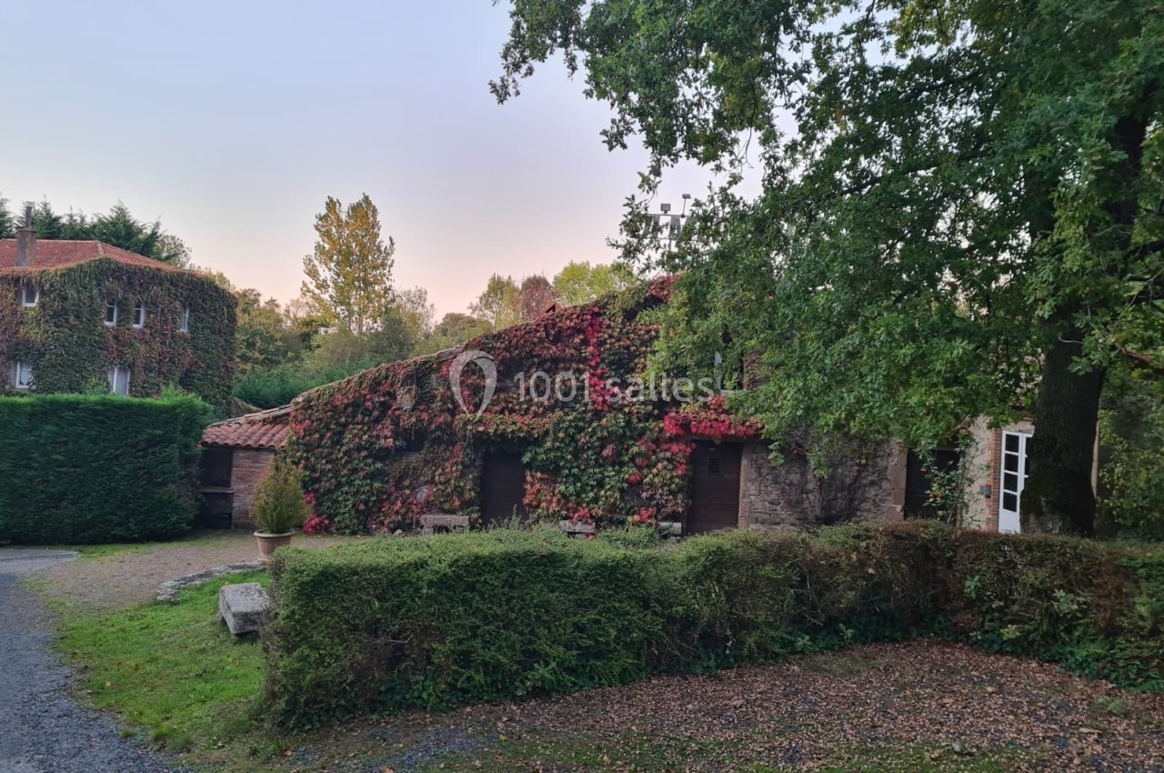 Maison en pierre recouverte de végétation automnale, entourée d'arbres et de haies dans un cadre naturel.