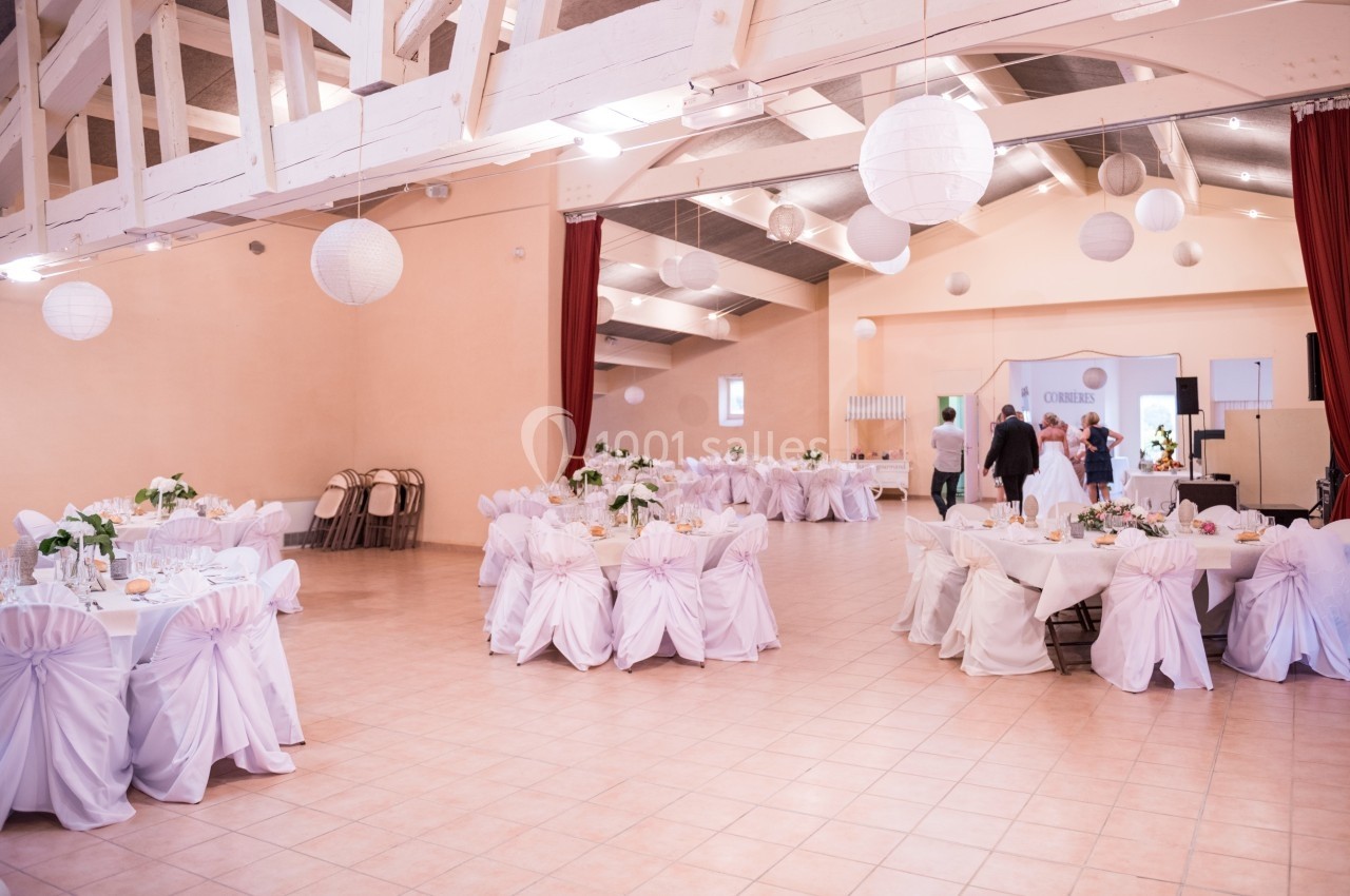 Salle de réception décorée avec des tables rondes nappées de blanc, chaises ornées de nœuds et lanternes suspendues.