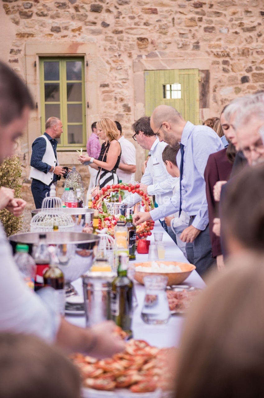 Des personnes se servent à un buffet en plein air, disposé sur une longue table devant un mur en pierre.