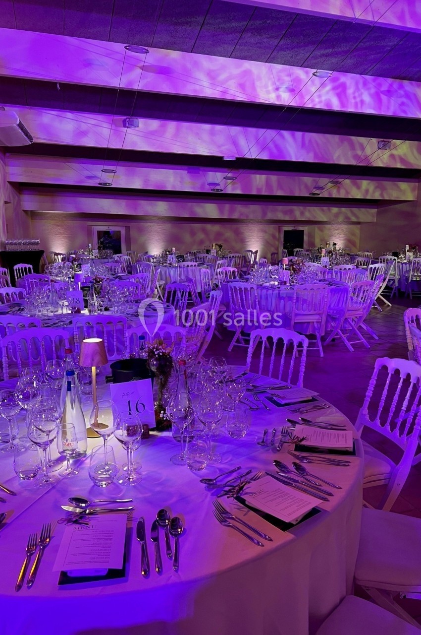 Salle de réception décorée avec des tables rondes élégamment dressées, éclairée par une lumière violette.