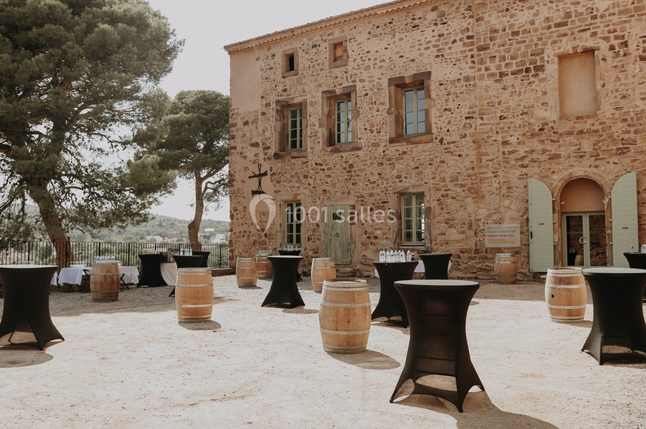 Cour extérieure d'un bâtiment en pierre avec tonneaux en bois et tables hautes noires, préparée pour un événement.