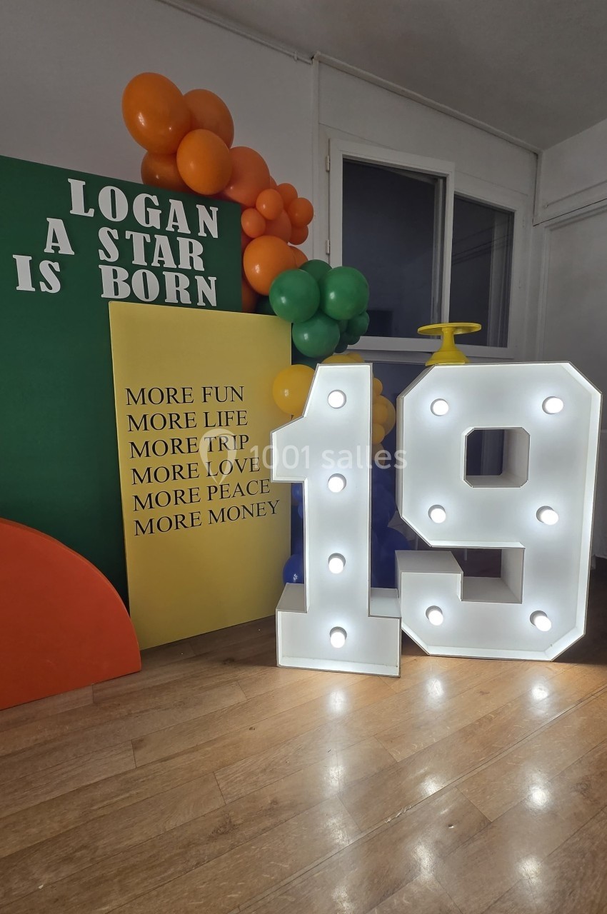 Décoration d'anniversaire avec le chiffre lumineux ’19’, ballons colorés et panneau avec messages inspirants.