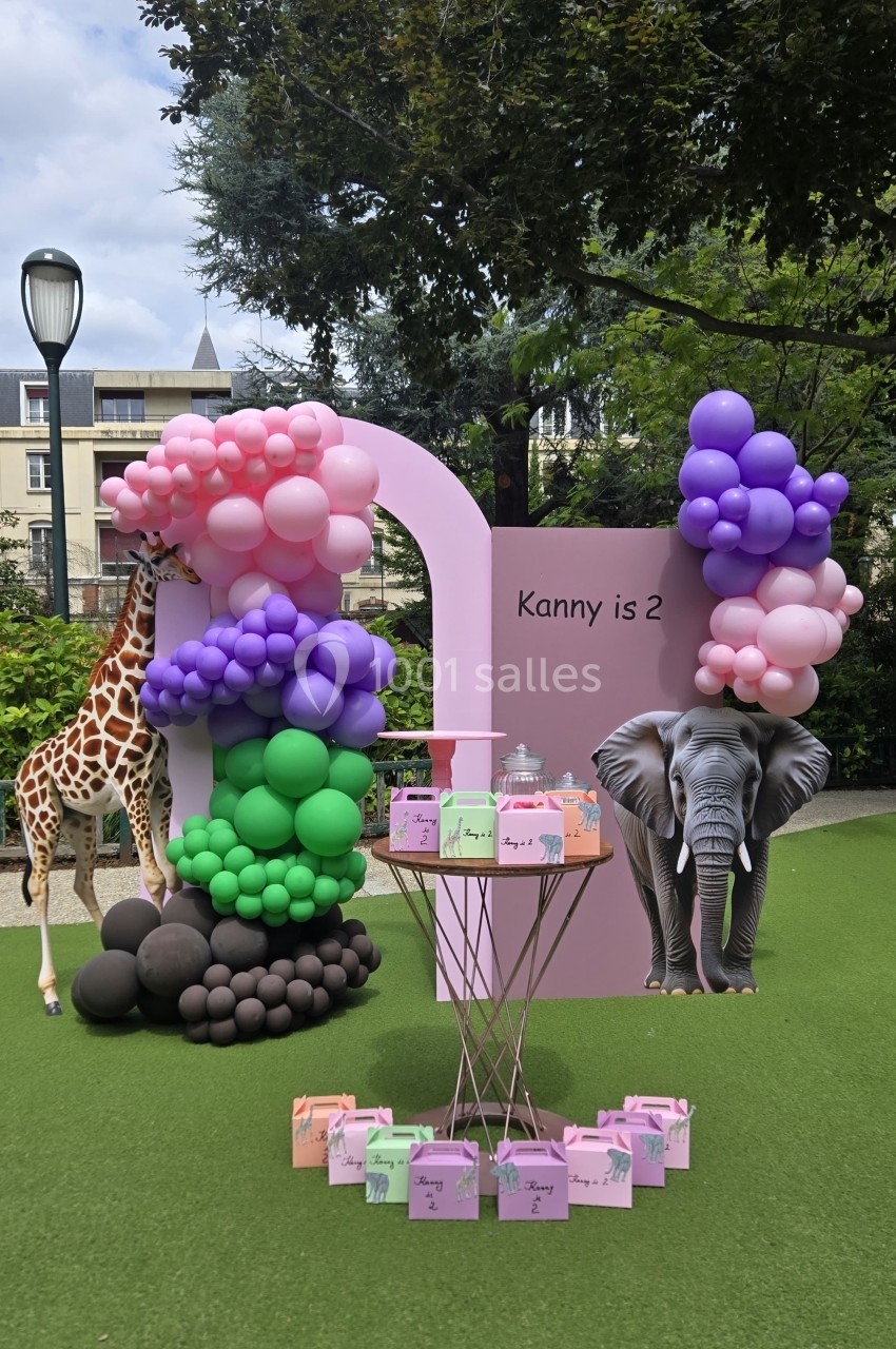 Décor de fête d'anniversaire avec ballons colorés, une girafe et un éléphant en carton sur fond de pelouse.