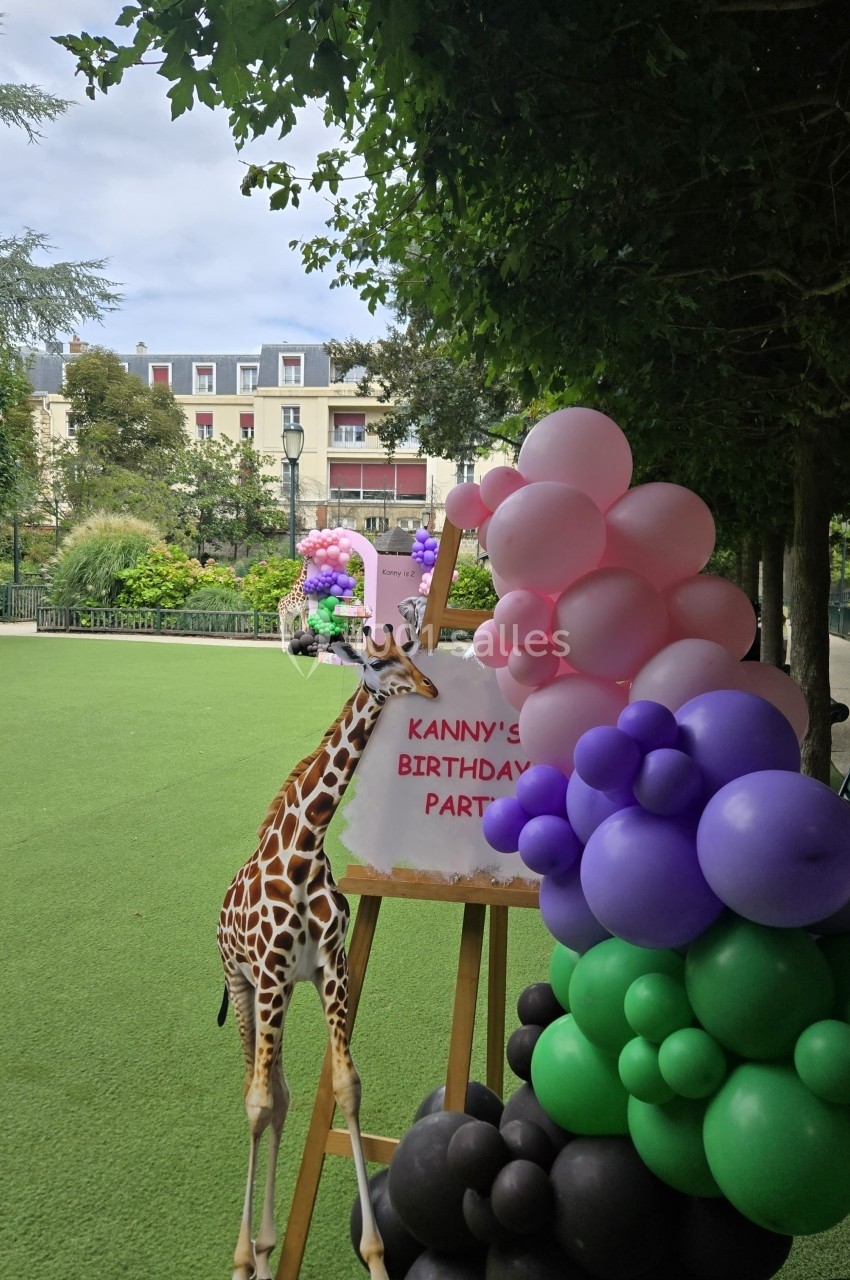Une girafe décorative près d'un panneau d'anniversaire entouré de ballons colorés dans un parc.