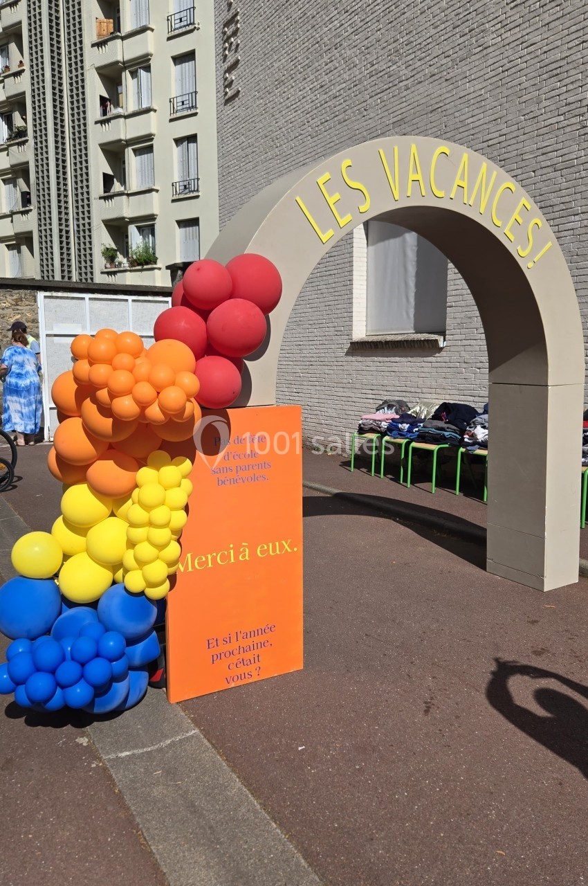Arche grise décorée de ballons colorés formant un arc-en-ciel, avec l'inscription ’Les vacances !’ en jaune.