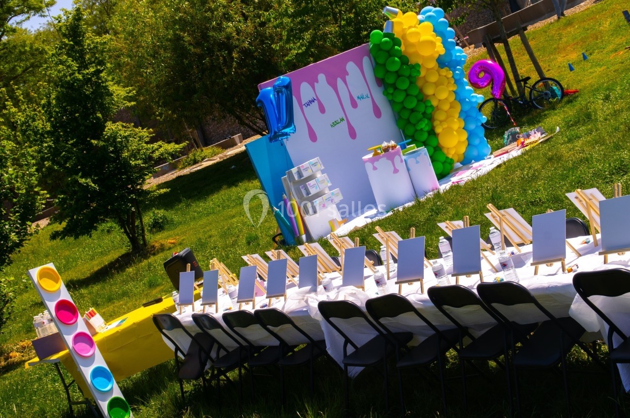 Tables alignées avec chevalets pour peinture en plein air, décor coloré avec ballons et panneaux artistiques.