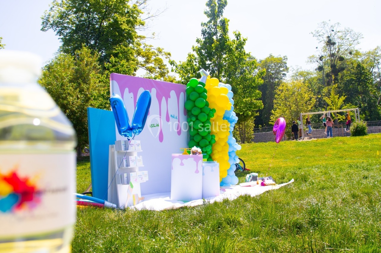 Stand décoré avec des ballons colorés et des panneaux, installé sur une pelouse lors d'un événement en plein air.
