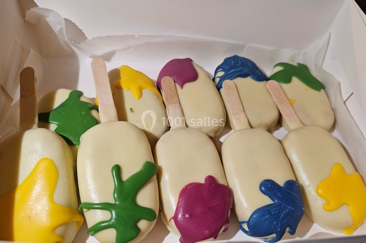 Glaces enrobées de chocolat blanc avec des éclaboussures colorées, disposées dans une boîte ouverte.