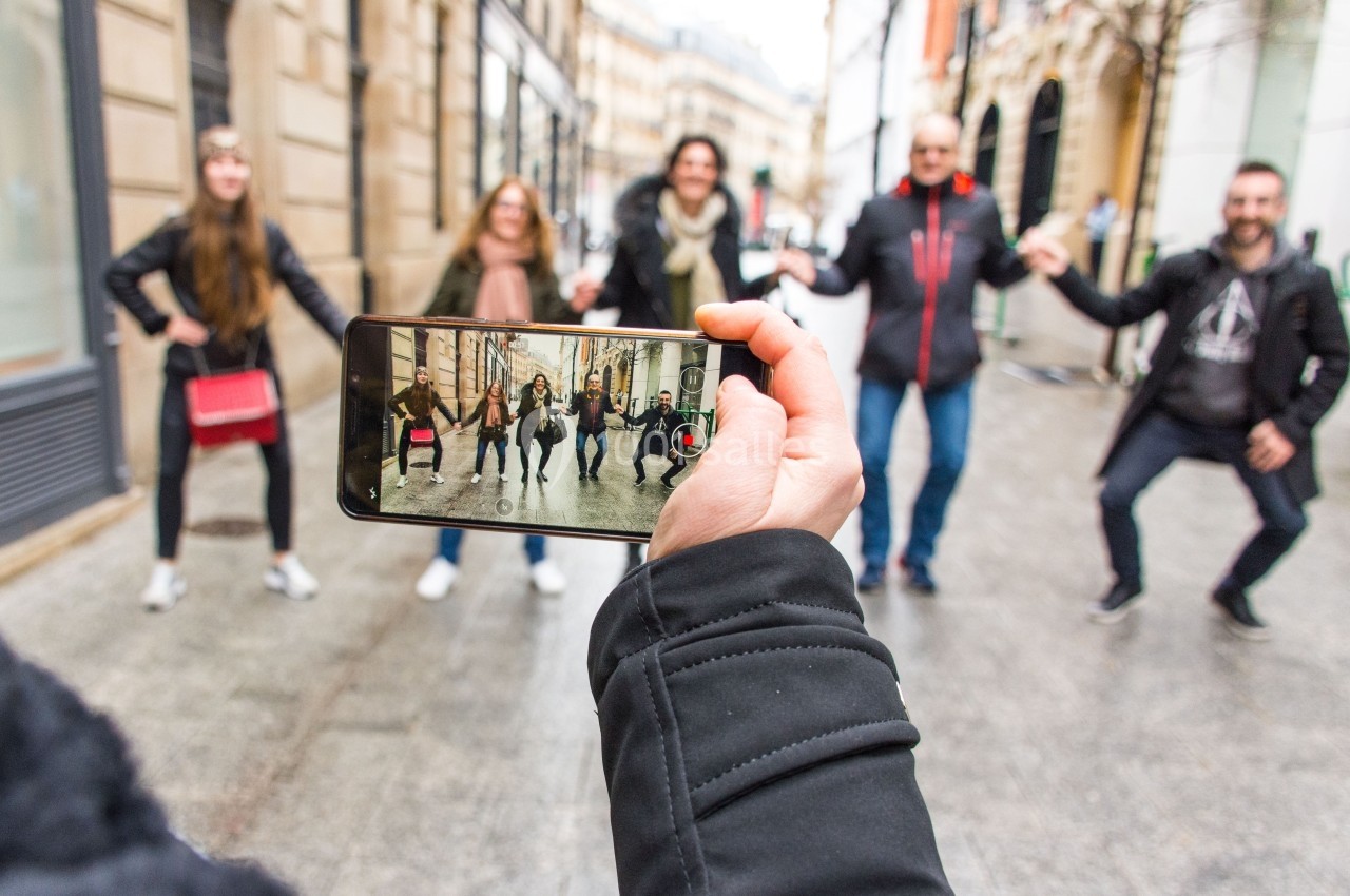 Une personne filme un groupe de cinq personnes dansant dans une rue urbaine avec un smartphone.