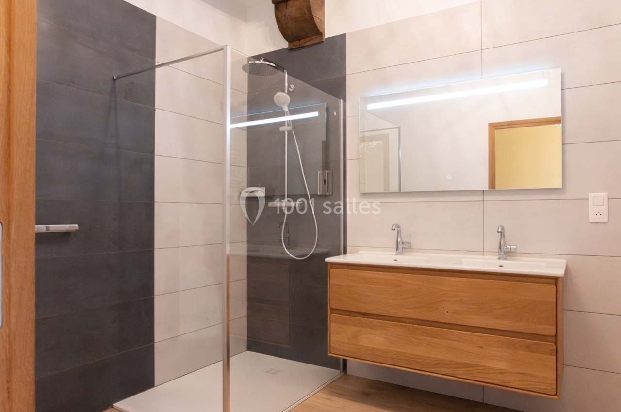 Salle de bain moderne avec douche à l'italienne, meuble en bois à double vasque et grand miroir éclairé.