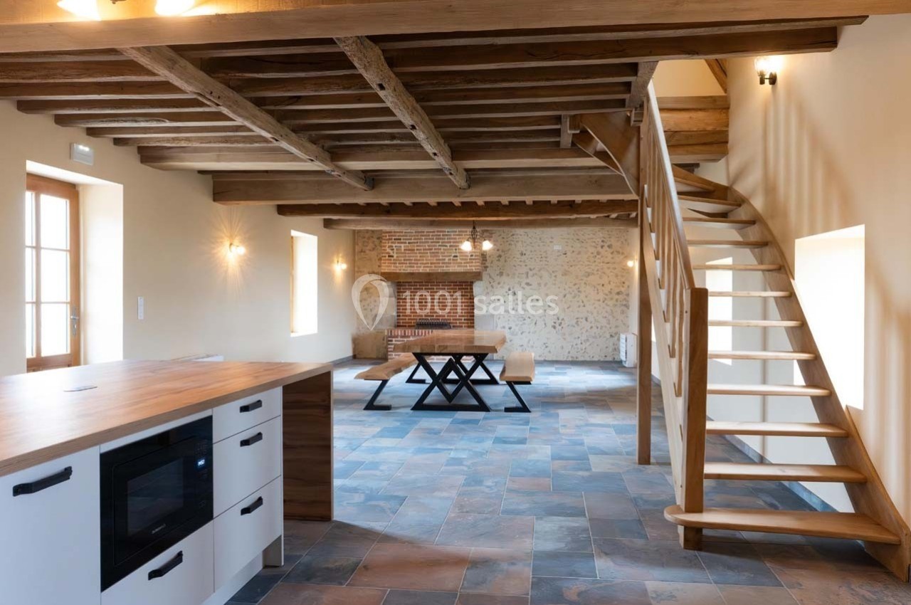Intérieur d'une maison rénovée avec poutres apparentes, escalier en bois, cuisine ouverte et table en bois massif.