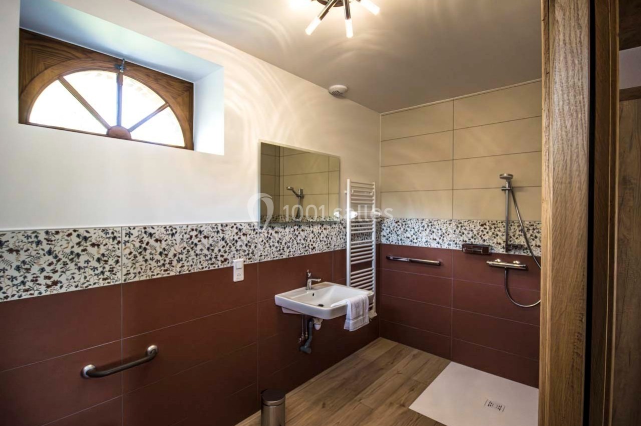 Salle de bain accessible avec douche à l'italienne, lavabo adapté, barre d'appui et éclairage naturel.
